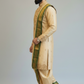 Man wearing a traditional beige and green sherwani against a plain background