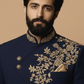 Man wearing a navy blue embroidered traditional outfit against a beige background