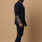 Man wearing a navy blue suit with gold embroidery on a beige background