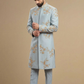 Man wearing a light blue embroidered sherwani against a beige background