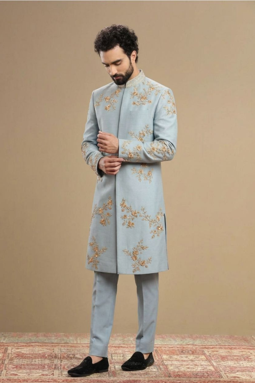 Man wearing a light blue embroidered sherwani against a beige background