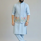 Man wearing a light blue kurta with an embroidered jacket on a plain background