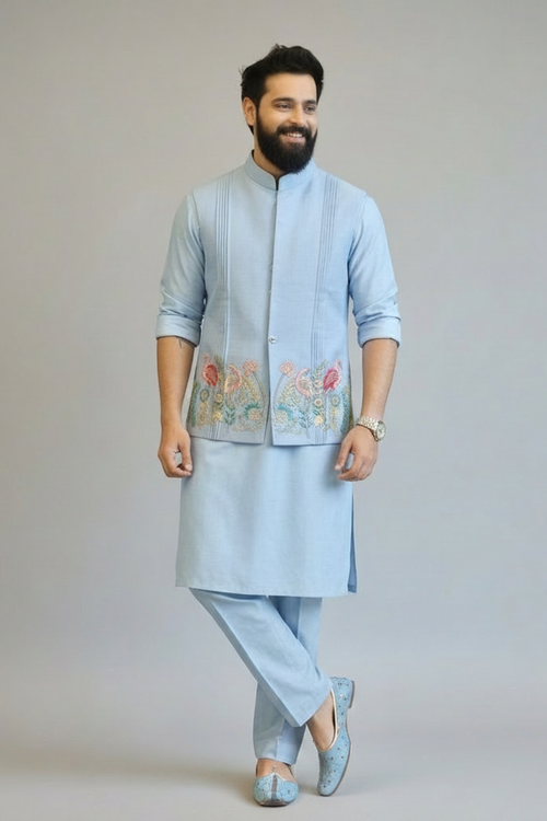 Man wearing a light blue kurta with an embroidered jacket on a plain background