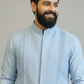 Man wearing a light blue traditional outfit with floral embroidery on a plain background