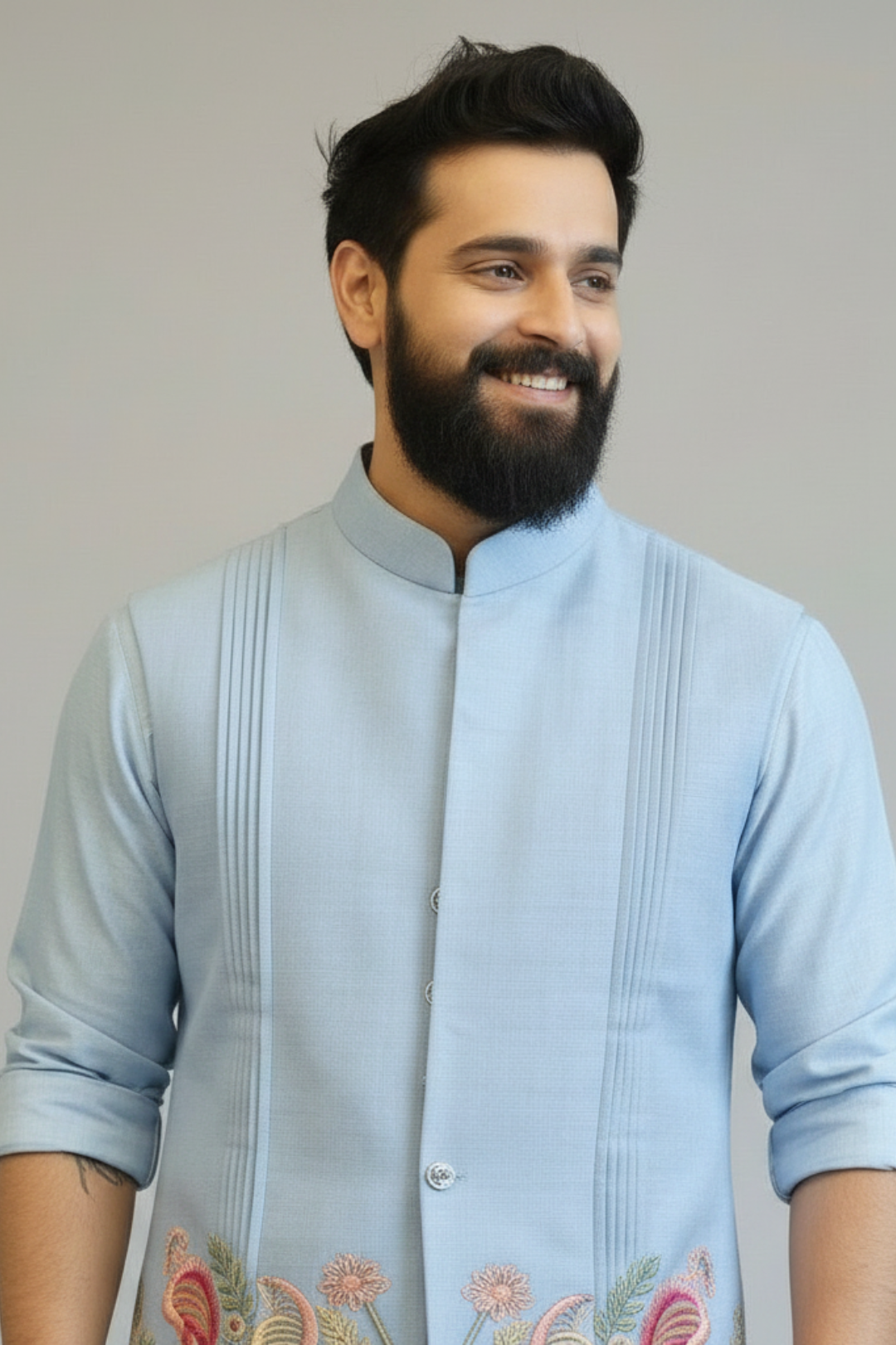 Man wearing a light blue traditional outfit with floral embroidery on a plain background