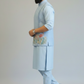 Man wearing a light blue traditional outfit with floral embroidery on a plain background