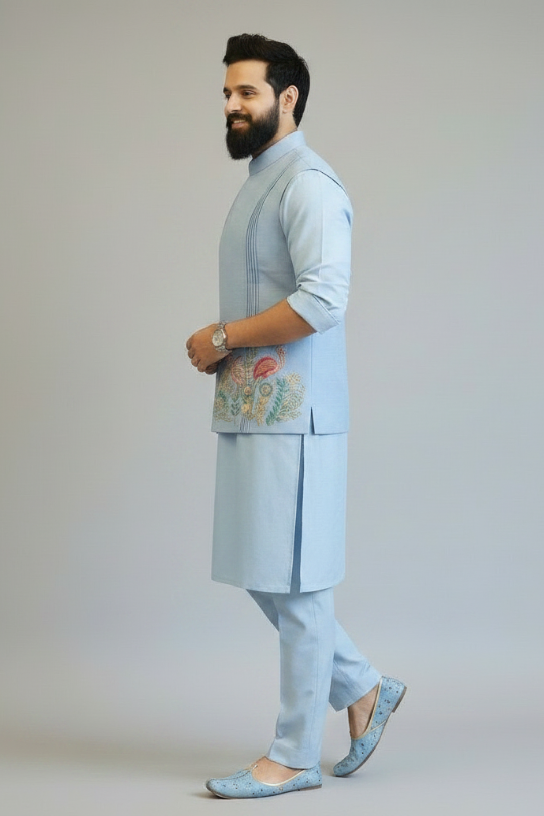 Man wearing a light blue traditional outfit with floral embroidery on a plain background
