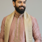 Man wearing a traditional pink kurta with a beige shawl against a plain background
