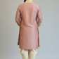 Man wearing a pink sherwani with white pants against a plain background