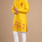 Man wearing a yellow kurta with floral embroidery and white pants on a beige background