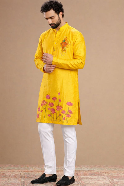 Man wearing a yellow kurta with floral embroidery and white pants on a beige background