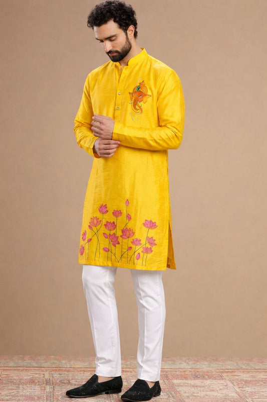 Man wearing a yellow kurta with floral embroidery and white pants on a beige background