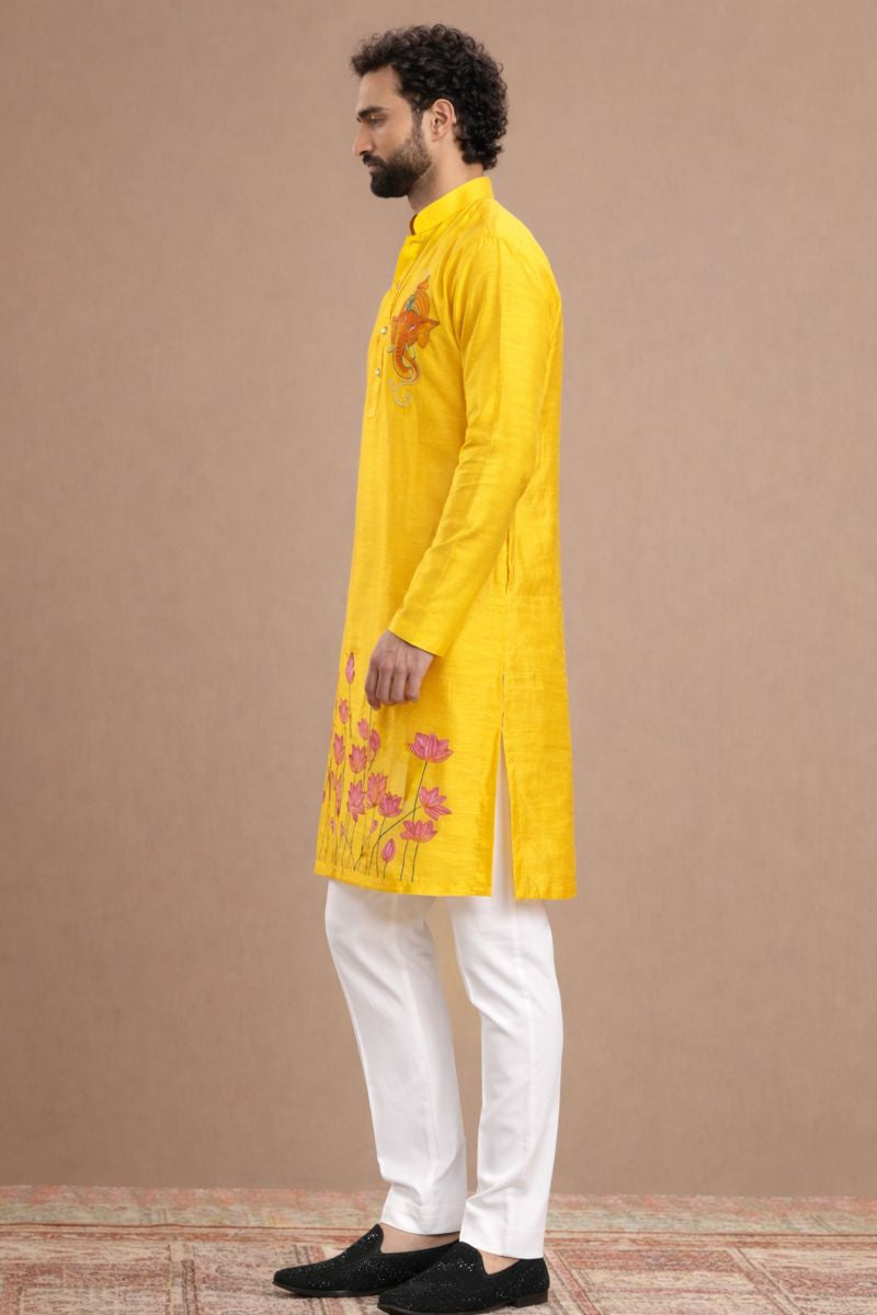 Man wearing a bright yellow kurta with white pants on a beige background