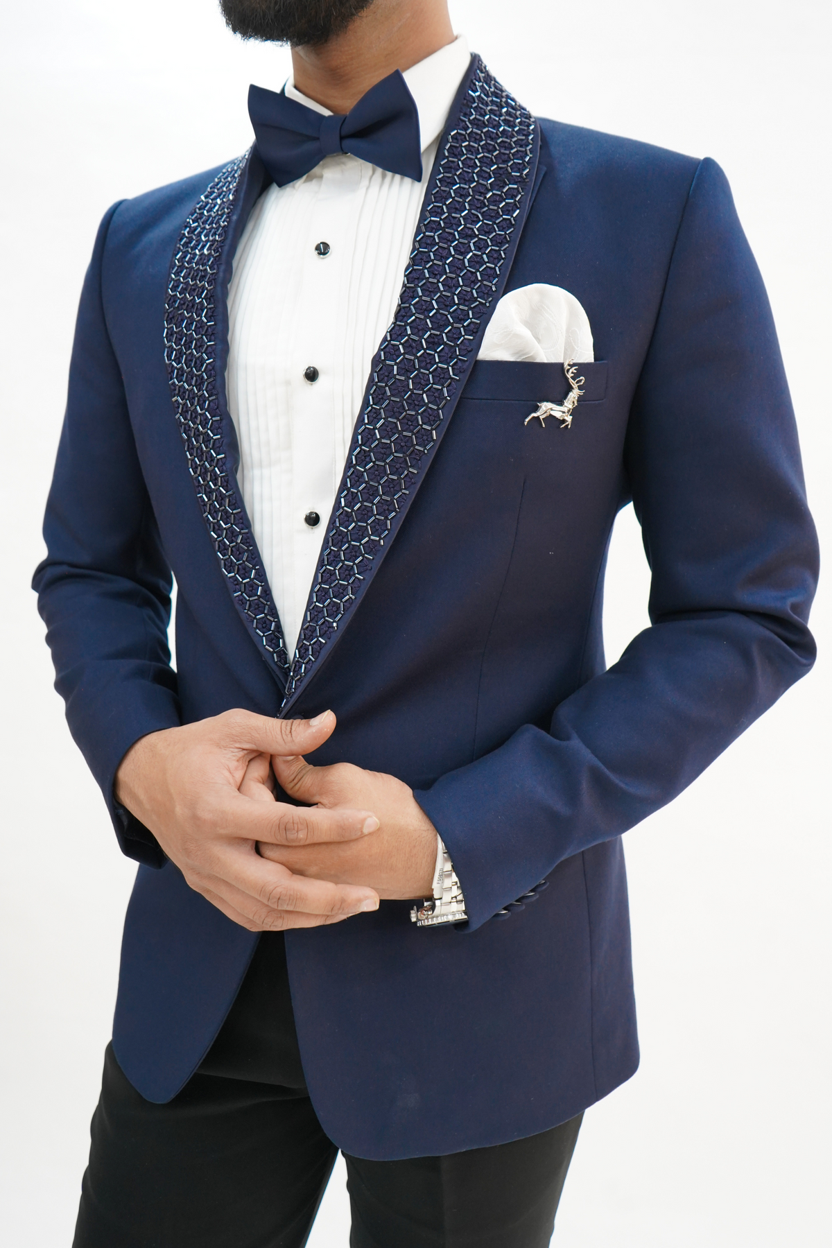 wearing a navy blue wool crepe 2-piece tuxedo with a detachable lapel, consisting of a jacket and trousers, accessorized with a bow tie and a handkerchief.