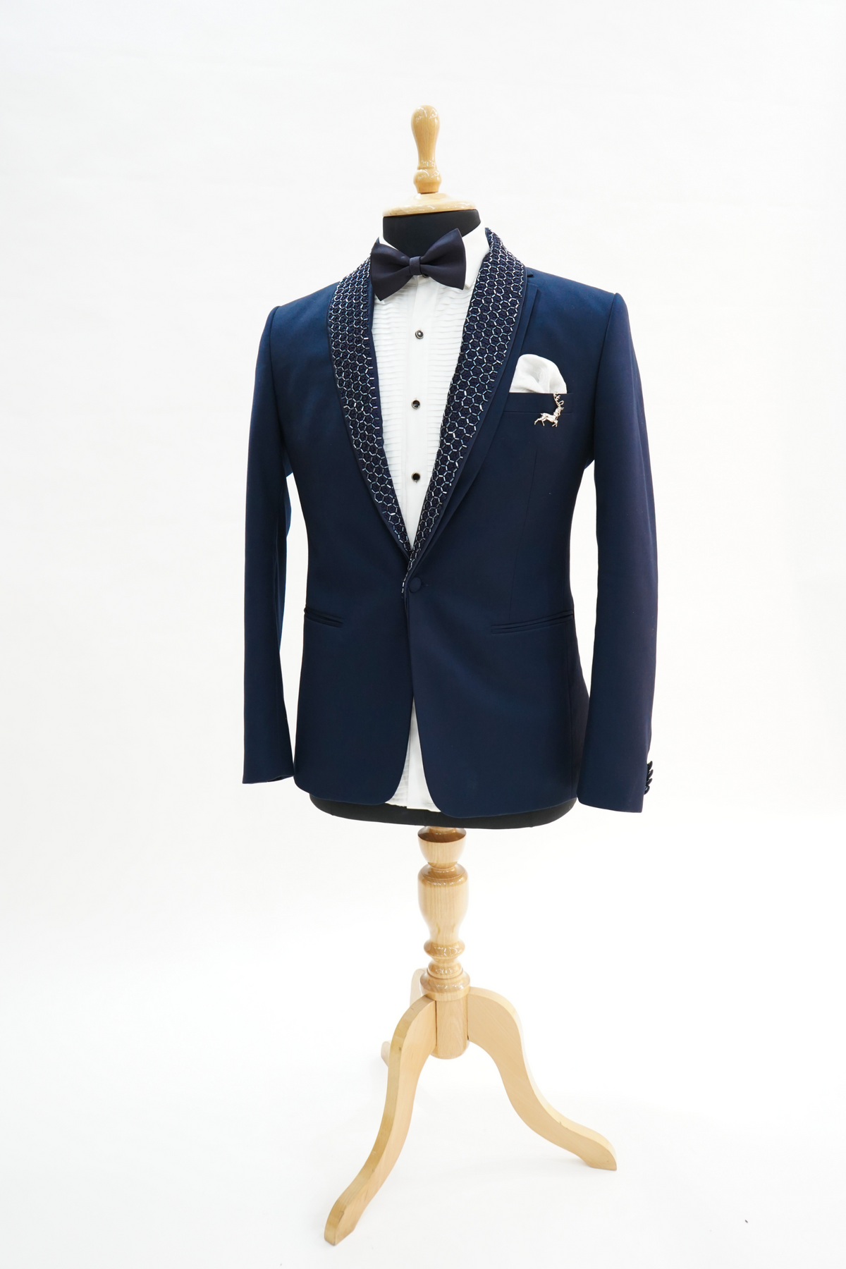 A man sitting on a yellow chair wearing a navy blue wool crepe 2-piece tuxedo with a detachable lapel, consisting of a jacket and trousers, accessorized with a bow tie and a handkerchief.