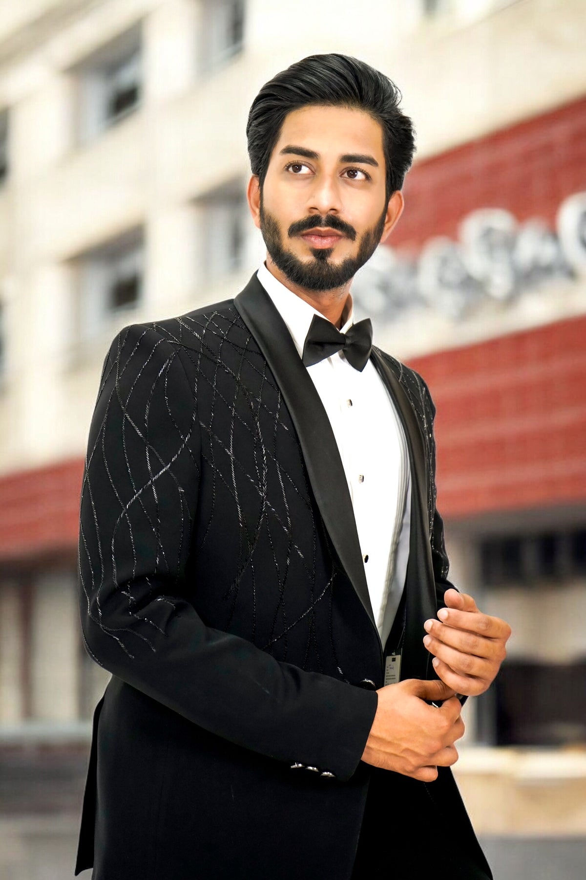 Man in a black tuxedo standing outdoors with a blurred background