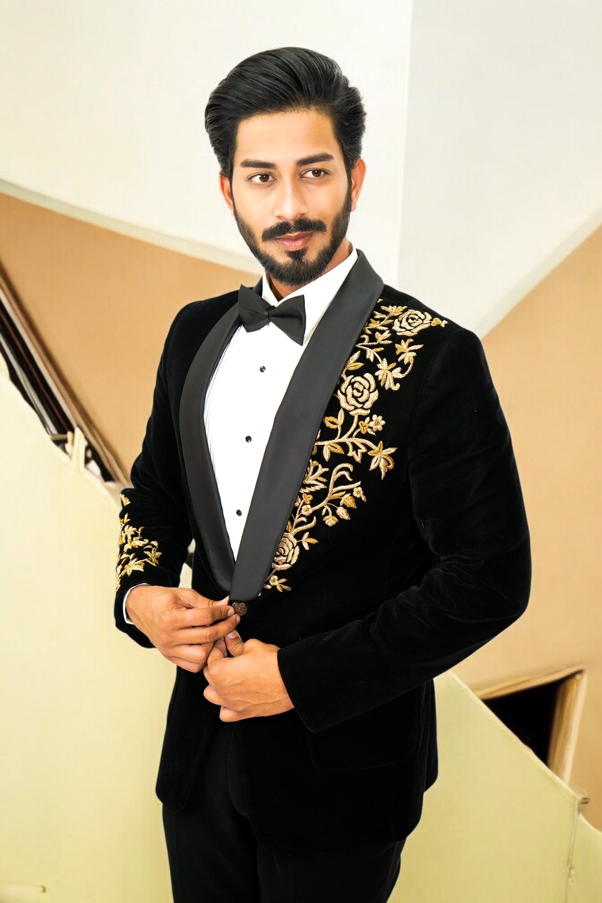 Man wearing a black tuxedo with gold embroidery in an indoor setting