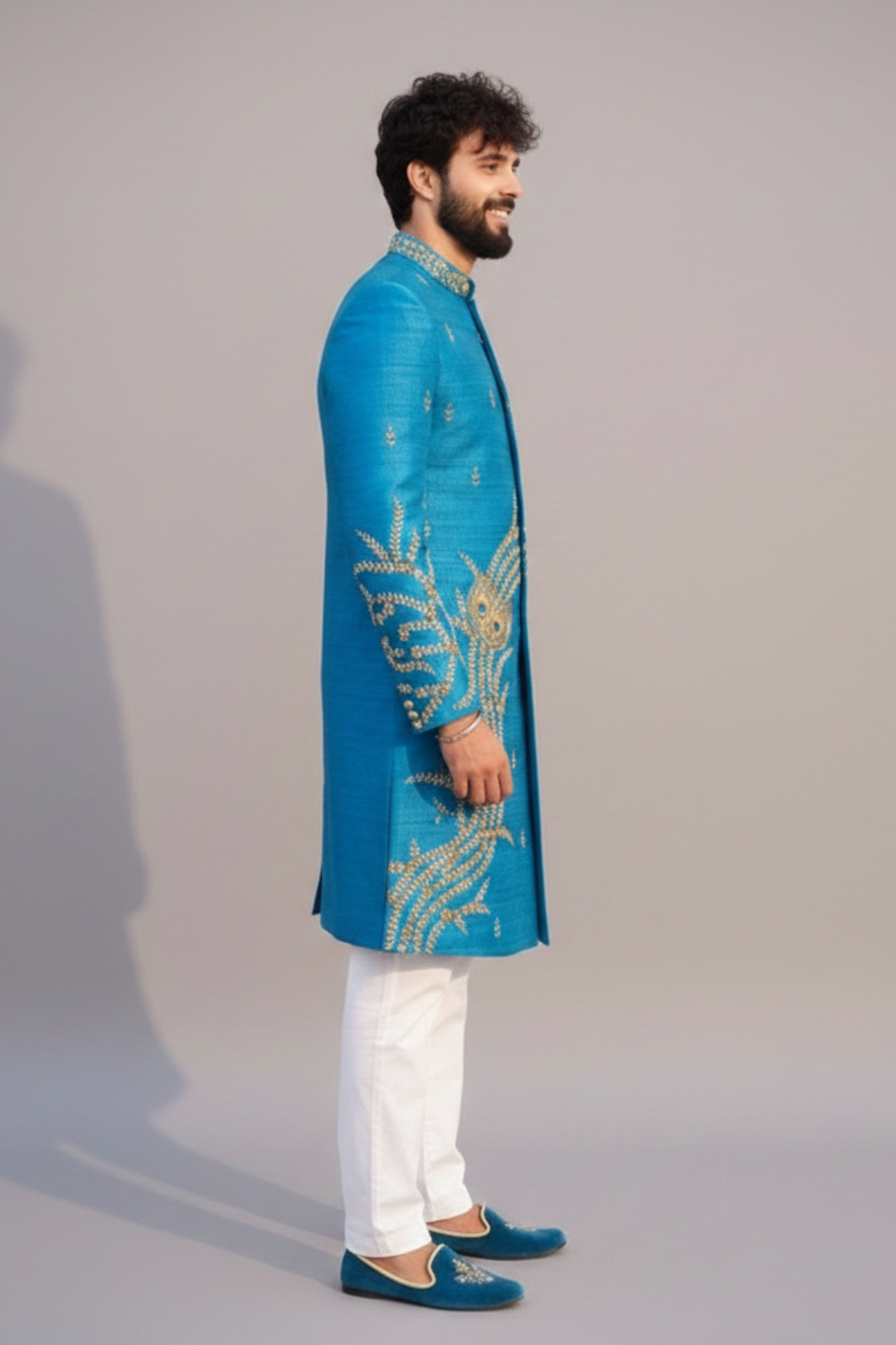 Man wearing a blue embroidered sherwani with white pants on a plain background