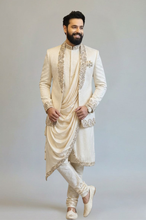 Man wearing a traditional cream sherwani with intricate embroidery on a plain background