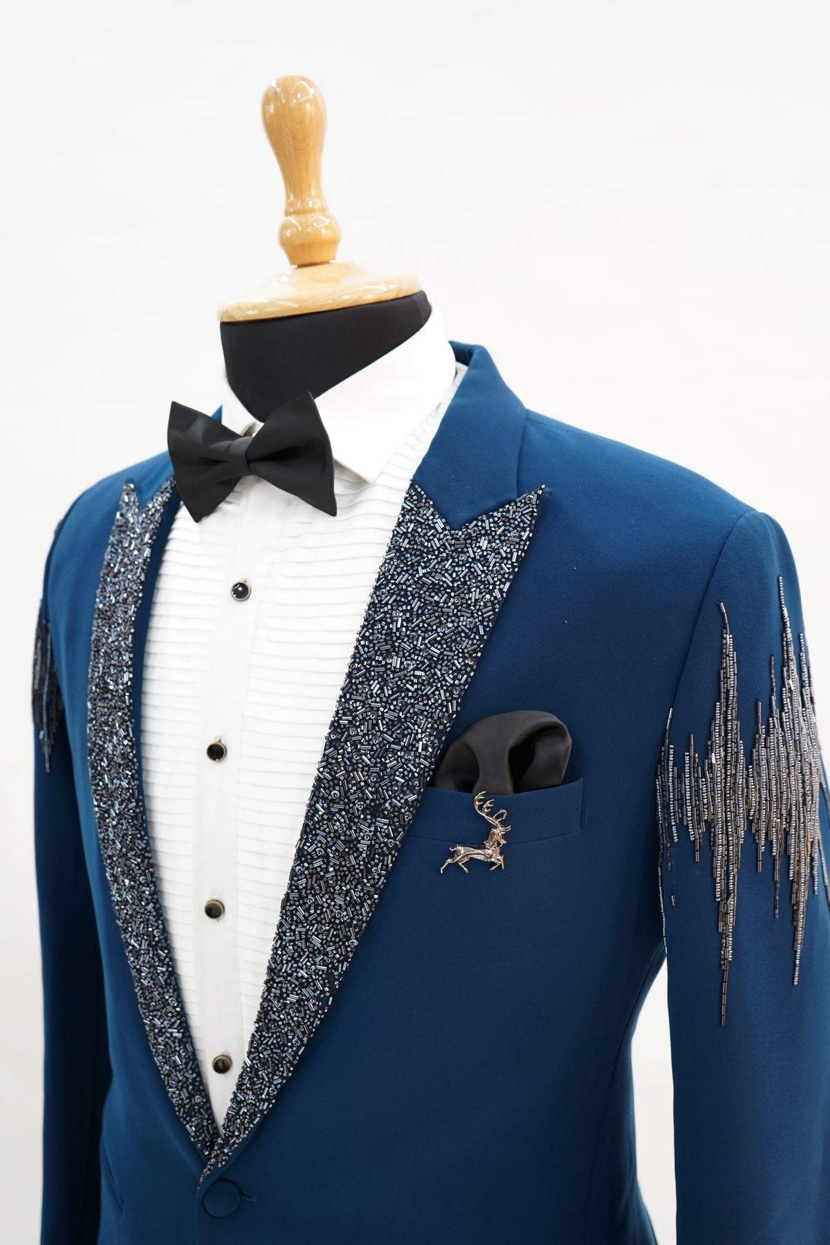 Man wearing a blue tuxedo with silver embroidery on a plain background