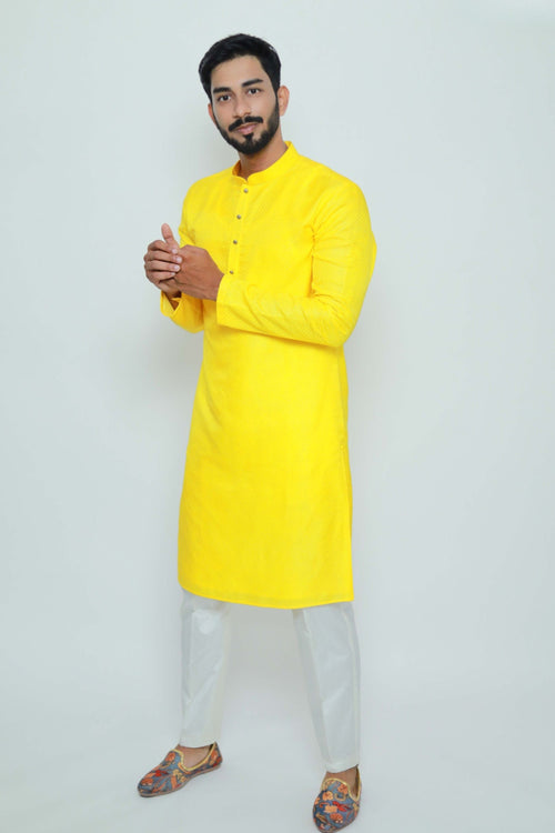 Man wearing a bright yellow kurta with white pants on a light gray background
