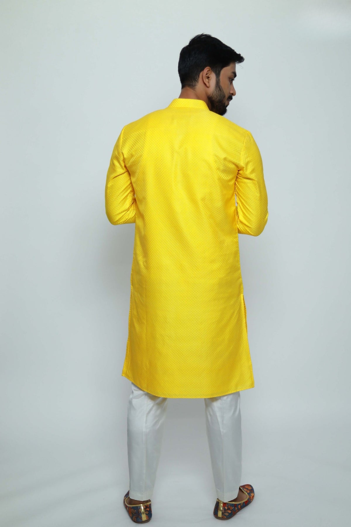 Man wearing a yellow kurta with white pants on a plain background