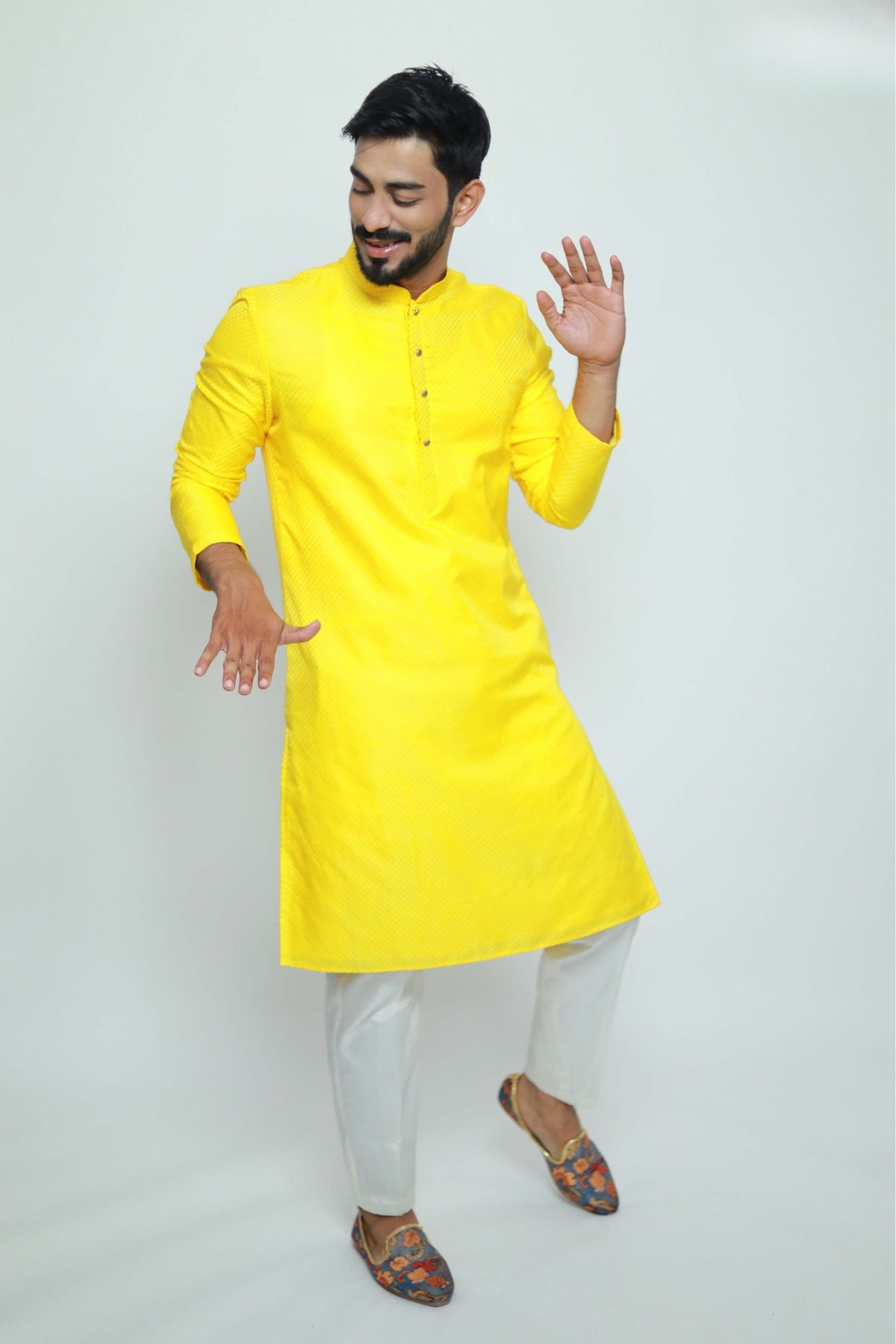 Man wearing a bright yellow kurta with white pants on a light gray background