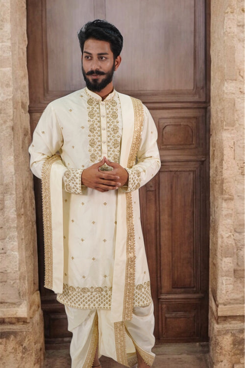 A man wearing a traditional beige wedding sherwani with floral embroidery and a mandarin collar.