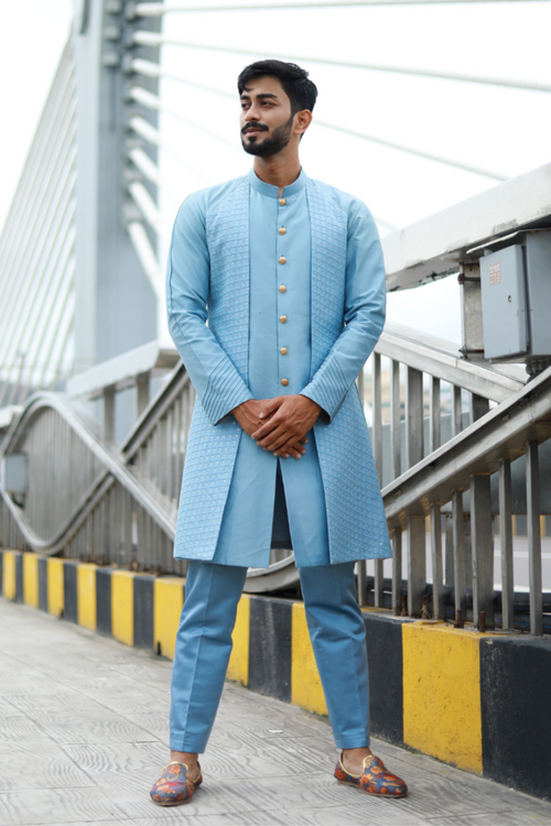 A man standing on a bridge wearing a blue Indo-Western Kurta with chikankari panels and pin tuck pleat details on the sleeves.