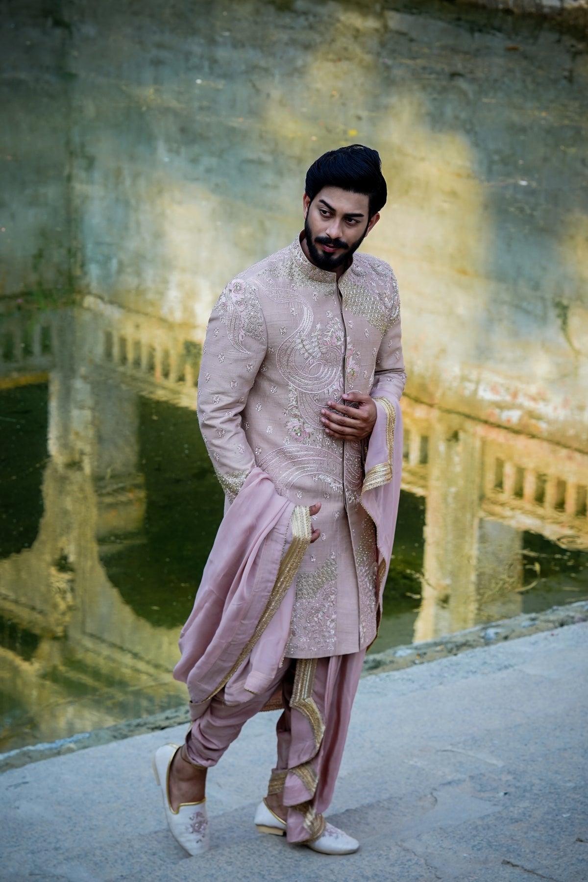 A man wearing a traditional Sherwani with premium silk dhoti and khandwa, featuring intricate embroidery and a pink tint.