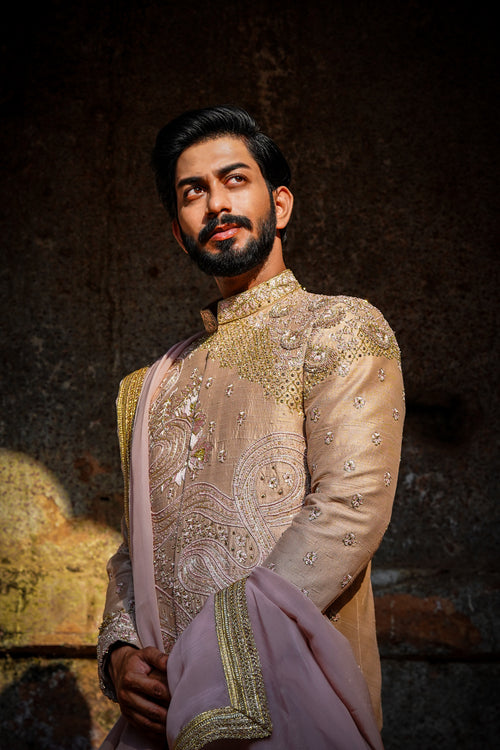 A man wearing a traditional Sherwani with premium silk dhoti and khandwa, featuring intricate embroidery and a pink tint.